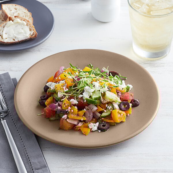 A tan matte porcelain coupe plate with a colorful salad served on it.