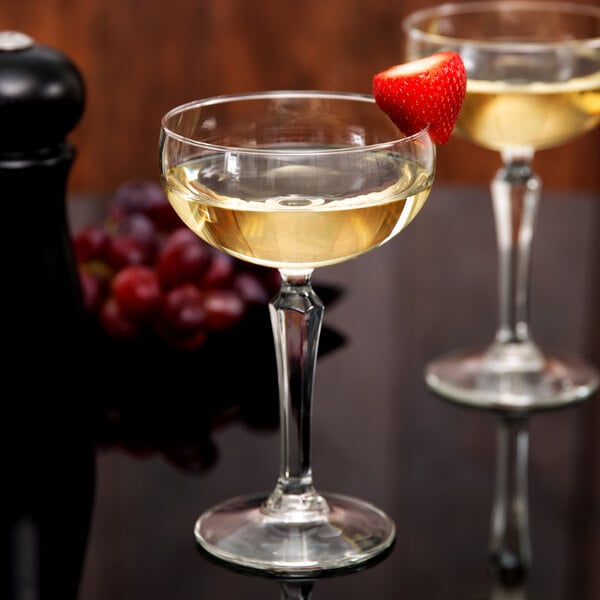 A clear Libbey Speakeasy 8.5 oz. coupe glass filled with a light-colored beverage and garnished with a strawberry on the rim.