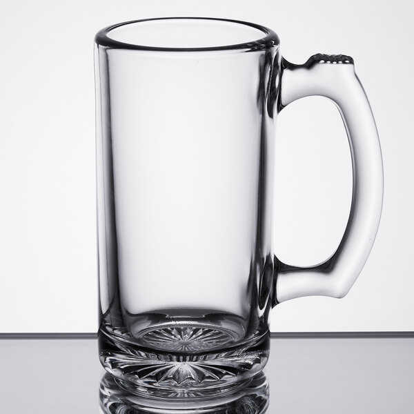 A clear glass beer mug with a sturdy handle and a patterned base.
