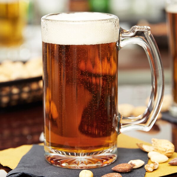 A clear glass 12 oz. beer mug filled with amber beer and topped with foam, placed on a napkin with assorted nuts nearby.