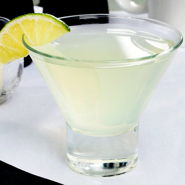 A clear Libbey Series V 7.6 oz. martini glass filled with a light-colored drink and garnished with a lime wedge.