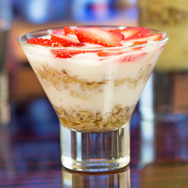 A clear Libbey Series V 7.6 oz. martini glass filled with layers of yogurt, granola, and sliced strawberries.
