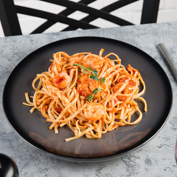 A black porcelain coupe plate holding a serving of pasta with shrimp and tomato sauce.
