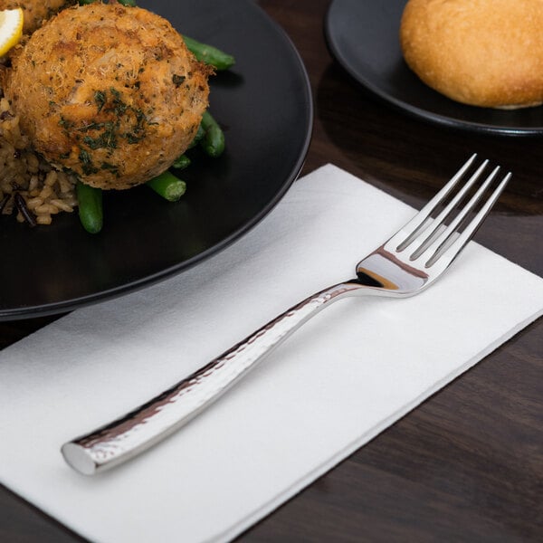 A stainless steel dinner fork with a textured handle placed on a white napkin.