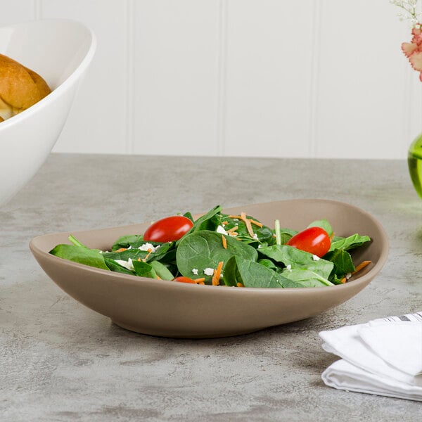 A sand-colored, matte porcelain coupe plate with an organic shape, shown holding a fresh salad.