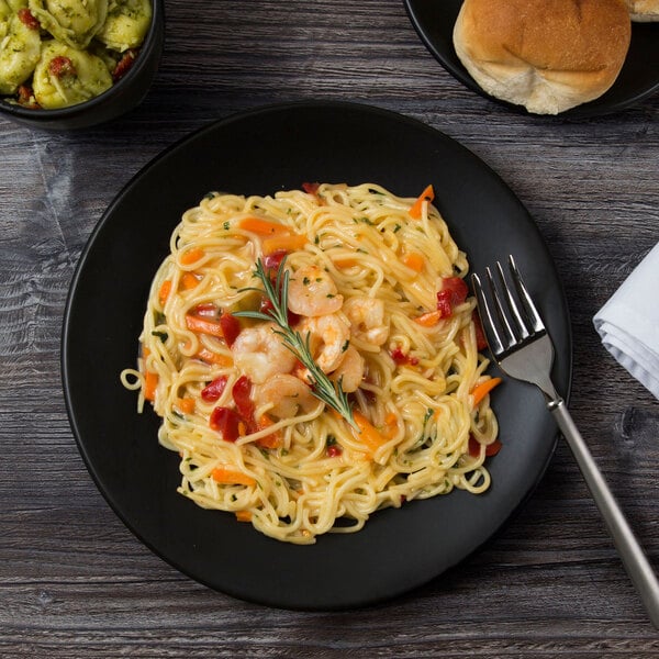 A black matte porcelain coupe plate holding a serving of pasta with shrimp and vegetables.