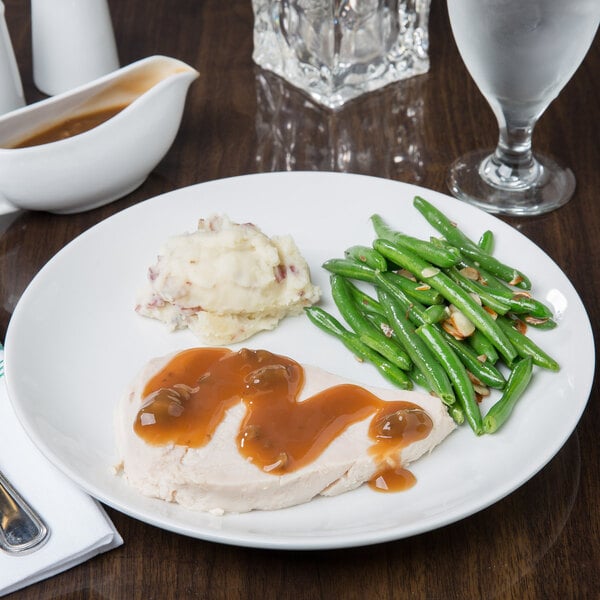 A white porcelain coupe plate holding sliced turkey with gravy, mashed potatoes, and green beans.