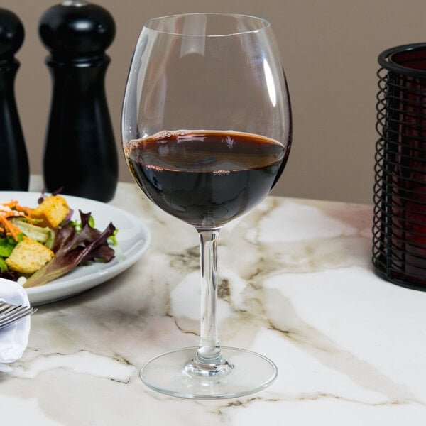 A clear balloon wine glass partially filled with red wine, placed on a marble table.