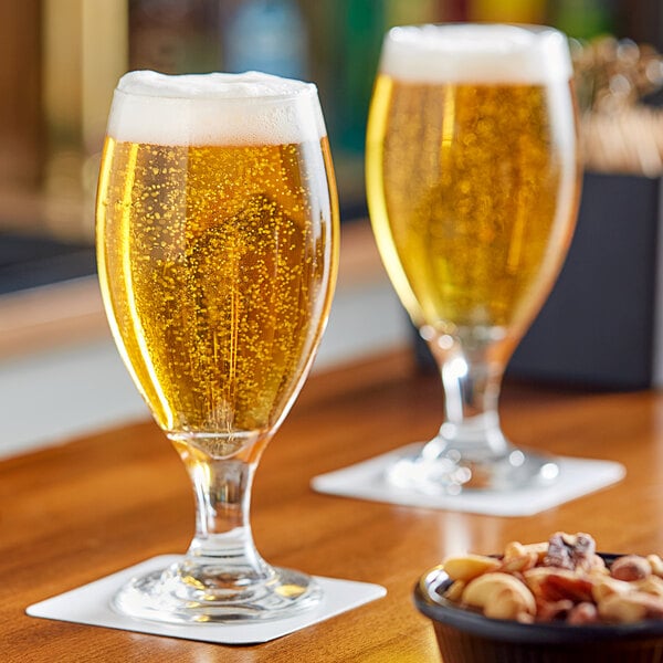 A clear stemmed pilsner glass filled with golden beer and topped with foam, placed on a coaster.