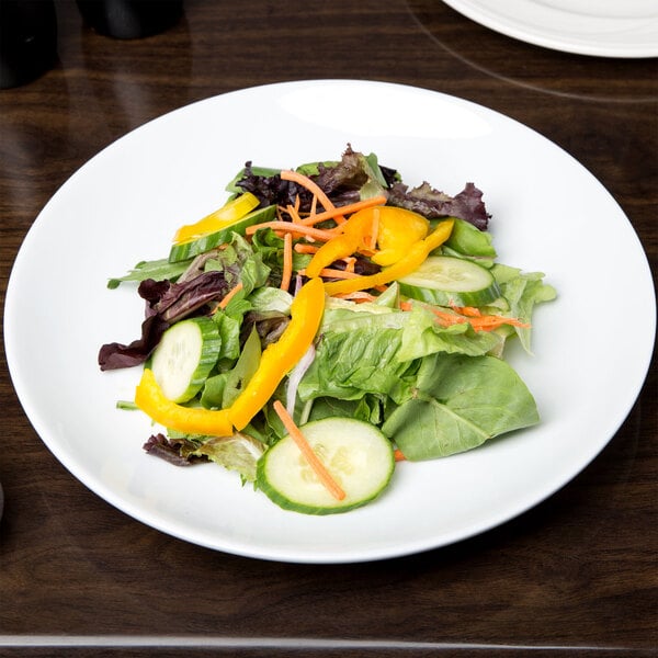 A white porcelain coupe plate with a mixed green salad featuring cucumbers, yellow bell peppers, and shredded carrots.