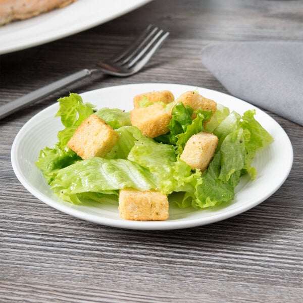 A small white porcelain coupe plate holding a simple salad with lettuce and croutons.
