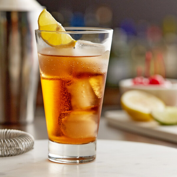 A clear 14 oz. highball glass filled with an iced beverage and garnished with a lemon wedge.
