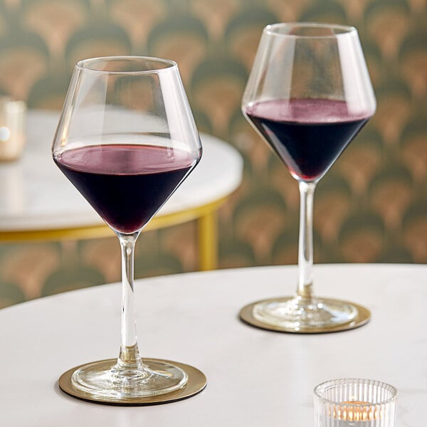 A pair of clear wine glasses partially filled with red wine, placed on a white table.