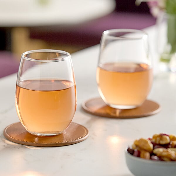 A pair of Libbey 9 oz. stemless wine glasses filled with rosÃ© wine, placed on round coasters on a table.