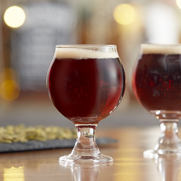 A small, round Belgian beer tasting glass filled with dark beer and a light foam head.