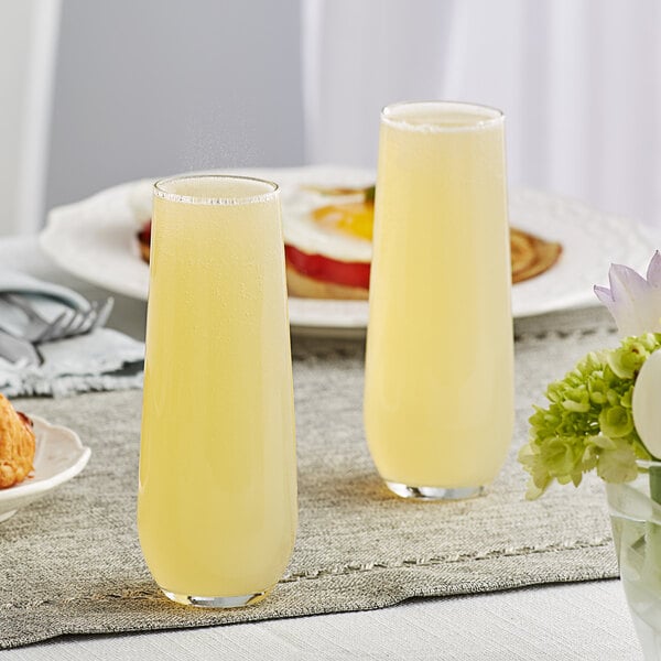 A pair of Libbey 8.5 oz. stemless flute glasses filled with a light yellow beverage on a breakfast table.