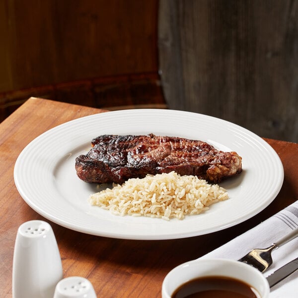 A white porcelain plate with a serving of grilled steak and a portion of rice.