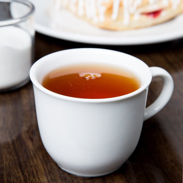 A white porcelain tea cup filled with tea, shown on a wooden table.