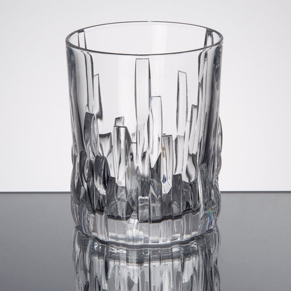 A clear glass rocks or double old fashioned glass with a textured, geometric design on the lower half.