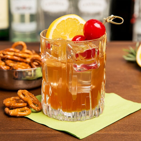 A clear, textured rocks glass filled with a cocktail, garnished with a lemon slice and cherries, placed on a green napkin.