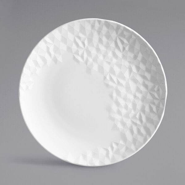 A white porcelain round coupe plate with a textured geometric pattern on part of the surface.
