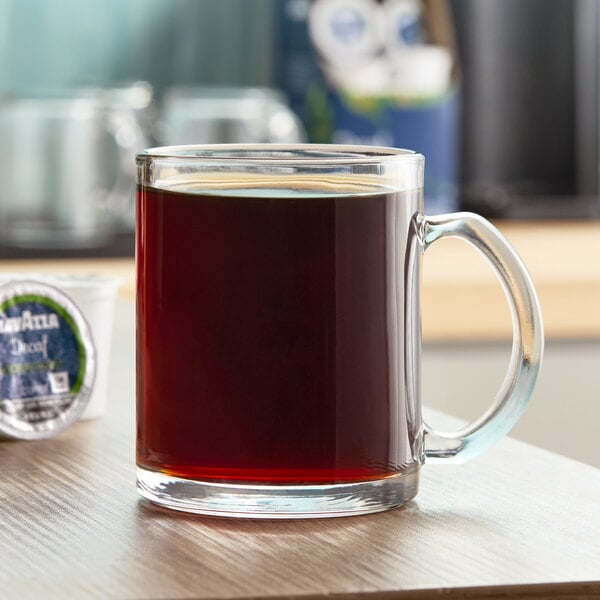 A clear glass mug filled with black coffee on a wooden surface.