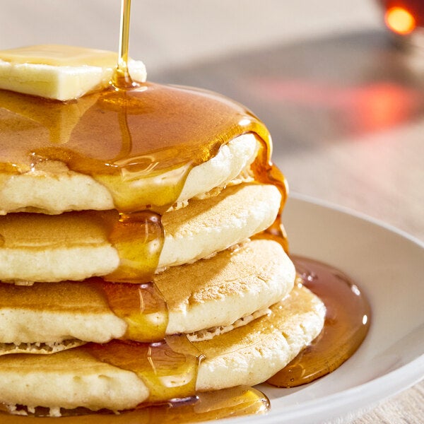 A stack of pancakes topped with butter and being drizzled with maple syrup on a white plate.