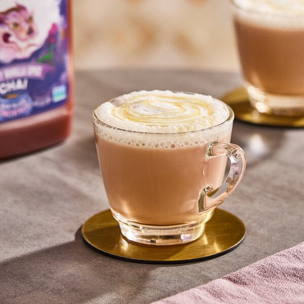 A glass cup filled with a frothy chai tea latte, placed on a gold coaster.