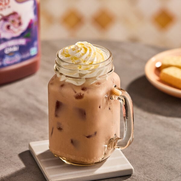 A glass mason jar filled with iced chai tea latte topped with whipped cream and a drizzle of honey.