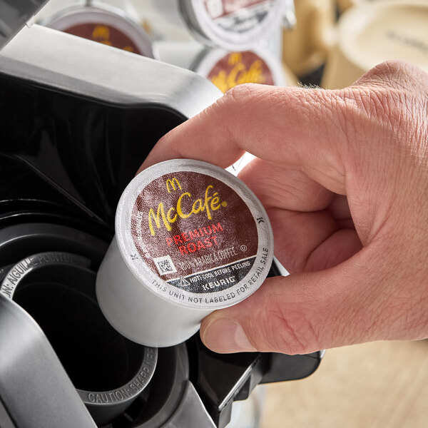 A McCafe Premium Roast Coffee single-serve Keurig K-Cup pod being placed into a coffee machine.