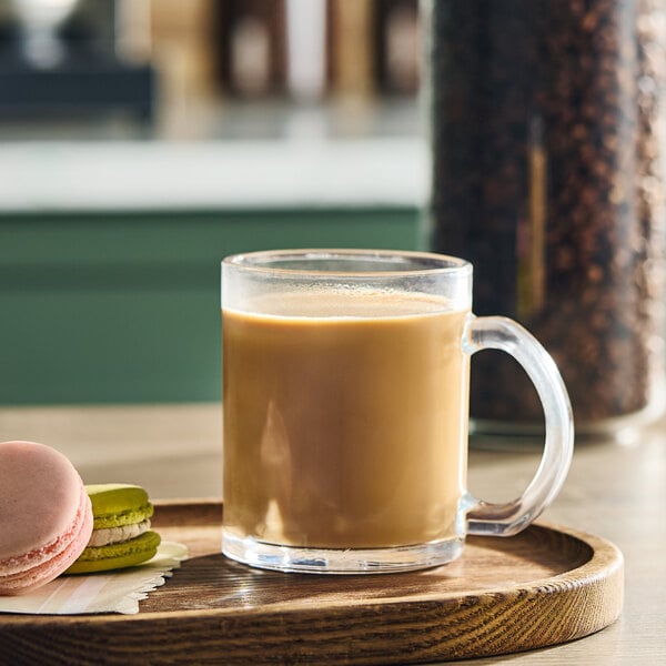 A clear glass mug filled with coffee sits on a wooden tray next to two macarons.