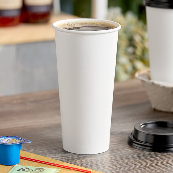 A plain white 24 oz. single wall paper hot cup filled with coffee, placed on a wooden surface.