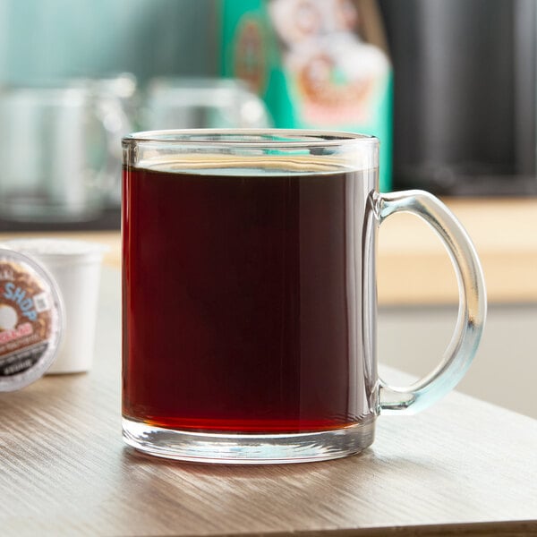 A clear glass mug filled with black coffee on a wooden surface.