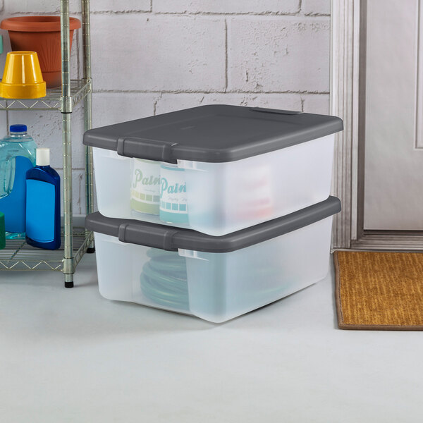 A pair of clear plastic storage totes with flat gray latching lids, stacked on the floor.