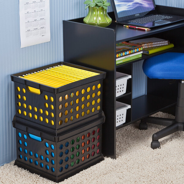 A black plastic storage crate with circular holes and colored handles, used for organizing files and office supplies.