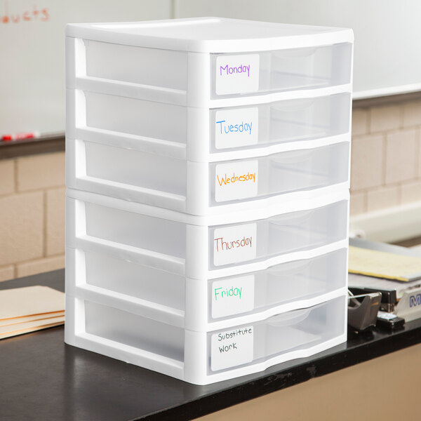 A white plastic countertop storage unit with six labeled drawers for organizing items by day of the week and substitute work.