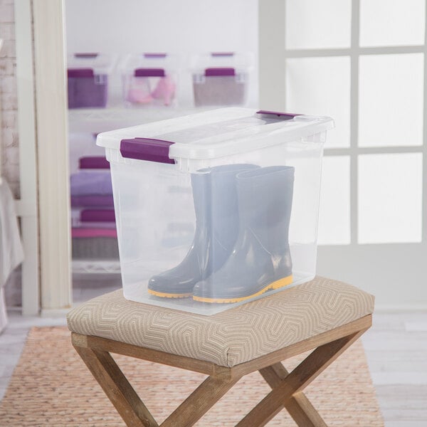 A clear plastic storage box with a lid and purple handles, containing a pair of boots.