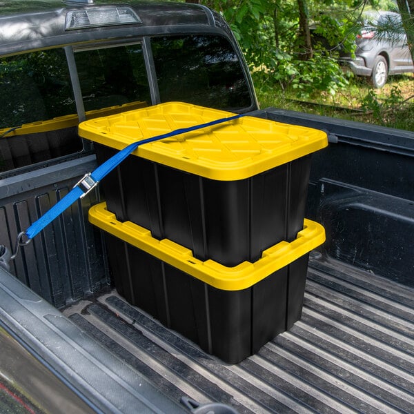 A pair of black industrial storage totes with yellow lids secured in the bed of a pickup truck.