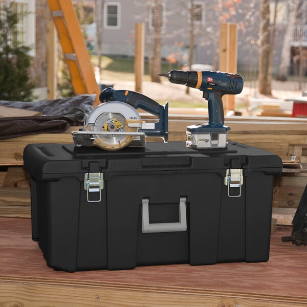 A large black Sterilite footlocker with metal latches and a gray handle, shown on a workbench with power tools on top.