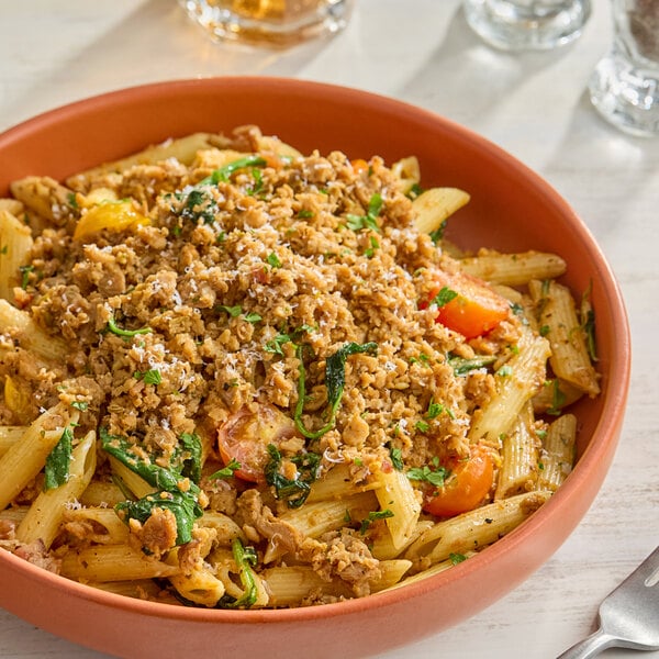 A bowl of penne pasta topped with MorningStar Farms plant-based vegan Italian sausage style crumbles and garnished with herbs.