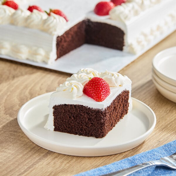 A slice of chocolate cake with white whipped icing and a strawberry on top, served on a white plate.