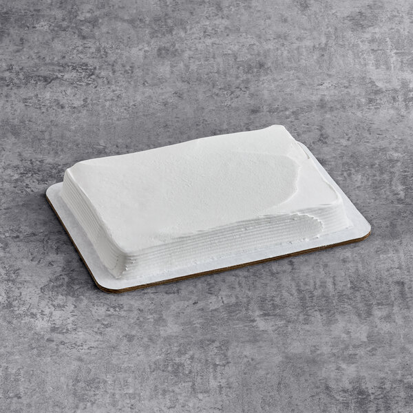 A rectangular yellow cake with smooth white whipped icing on a cardboard base.