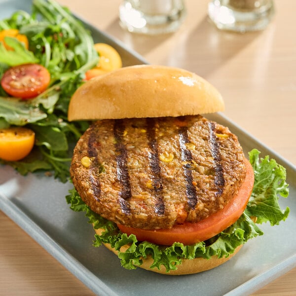 A plant-based vegan veggie burger with lettuce and tomato on a bun, served with a side salad.