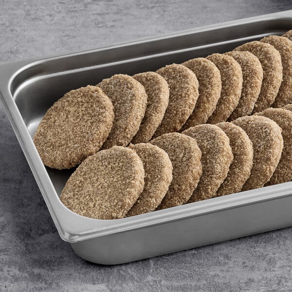 A stainless steel tray filled with several breaded, plant-based vegan patties arranged in rows.