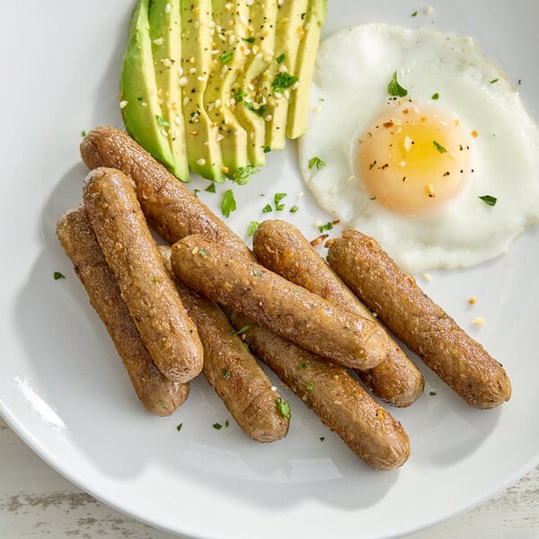 A plate of plant-based vegetarian breakfast sausage links served with sliced avocado and a fried egg.