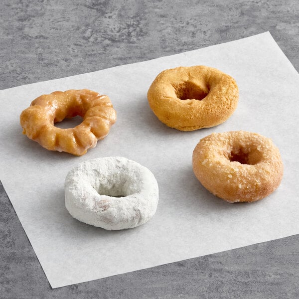 An assortment of four cake donuts, each with a different coating or glaze, displayed on a sheet of parchment paper.