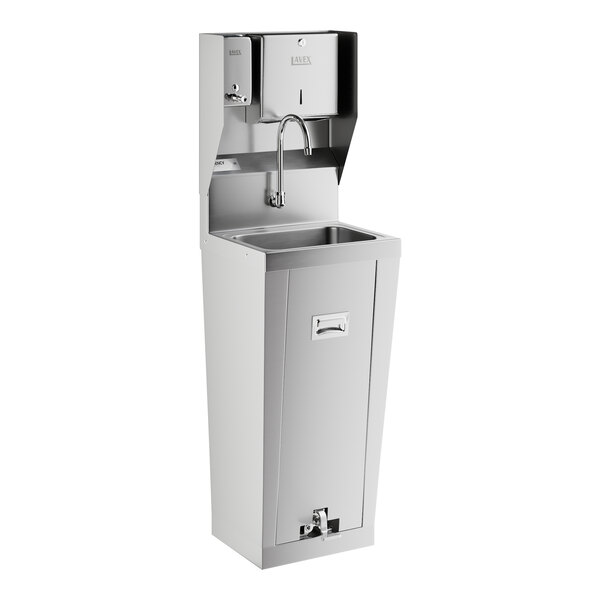 A stainless steel hands-free hand sink with a pedestal base, foot pedal, paper towel dispenser, and soap dispenser.