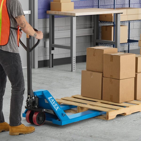 A blue manual pallet jack being used to move a wooden pallet loaded with cardboard boxes in a warehouse setting.