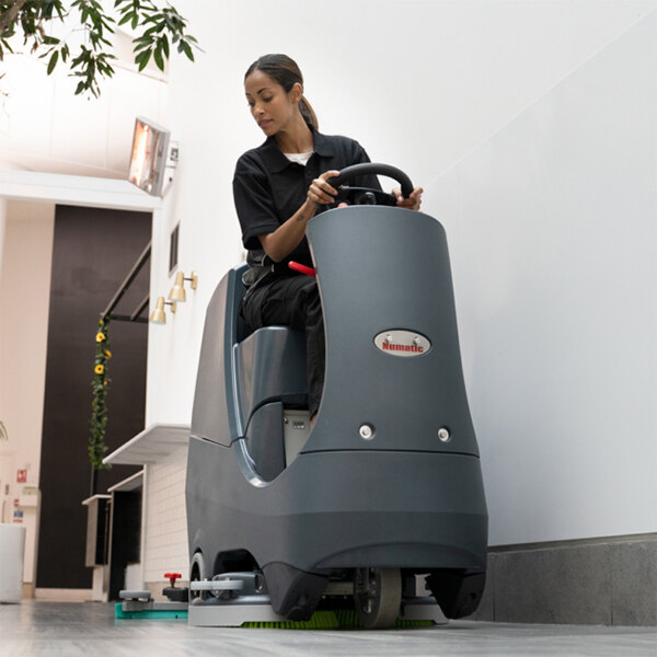 A ride-on floor scrubber machine being operated indoors.