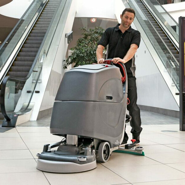 A commercial floor scrubber machine being operated by a person in a shopping mall.